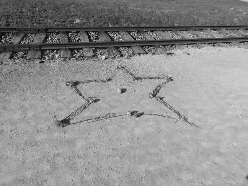 Vor einem Bahngleis ist aus Nelken ein Stern auf eine Sand-Schotterfläche gelegt. In der Mitte des Sterns befindet sich ein länglich-runder Stein mit der Aufschrift 10.4.2015